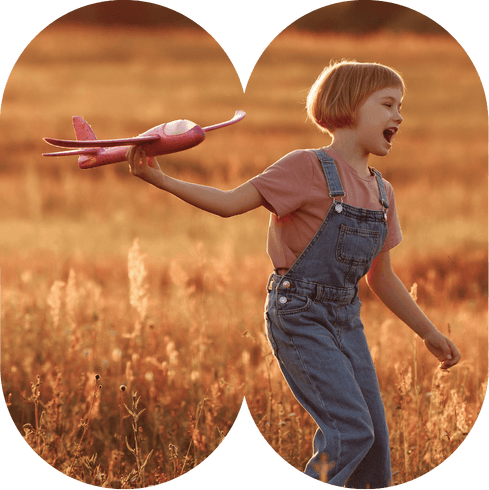 Enfant jouant dans un champ avec un avion en papier dans le main imitant le décollage